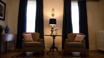 A room with two armchairs, a small table with a lamp, and a large window with curtains.
