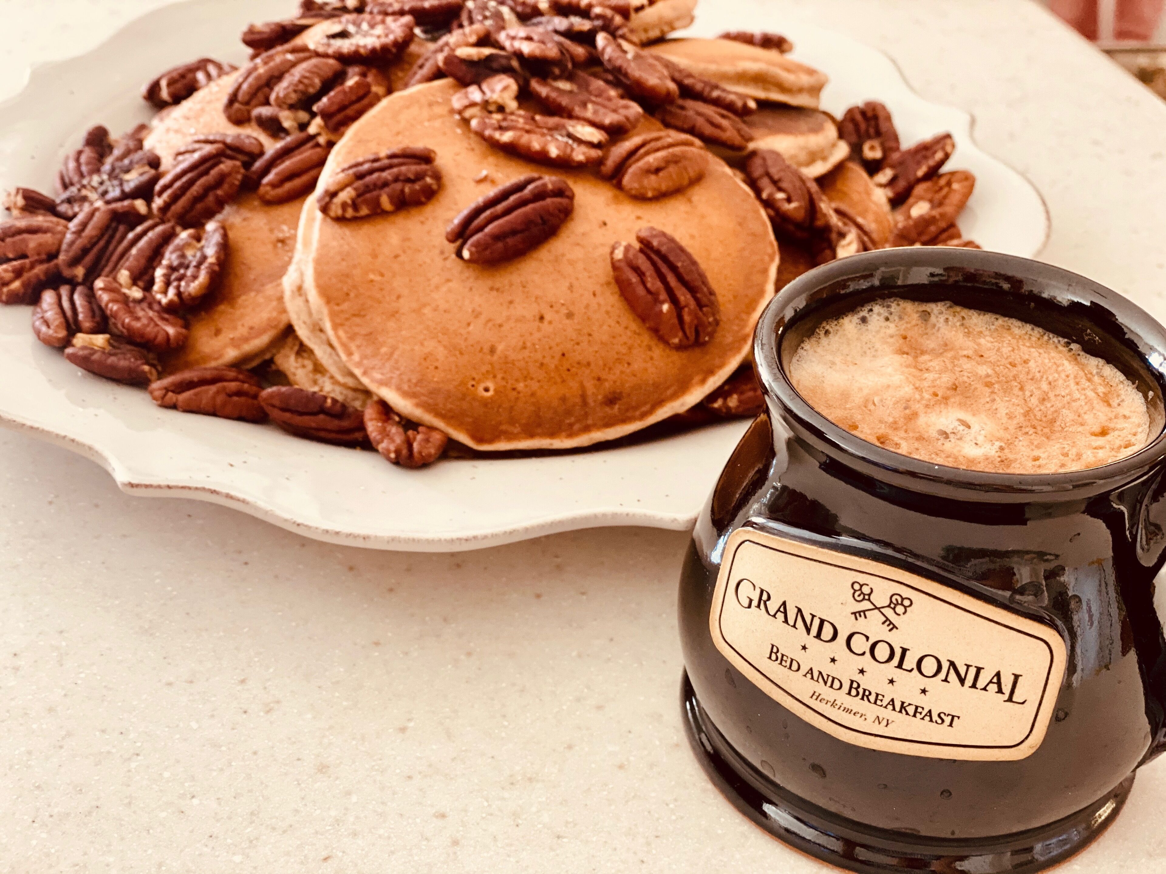 A plate of pancakes topped with pecans and a jar labeled "Grand Colonial Bed and Breakfast."