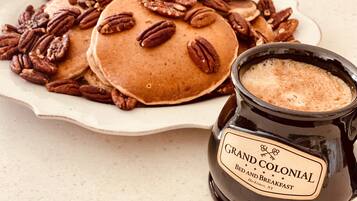 A plate of pancakes topped with pecans and a jar labeled "Grand Colonial Bed and Breakfast."