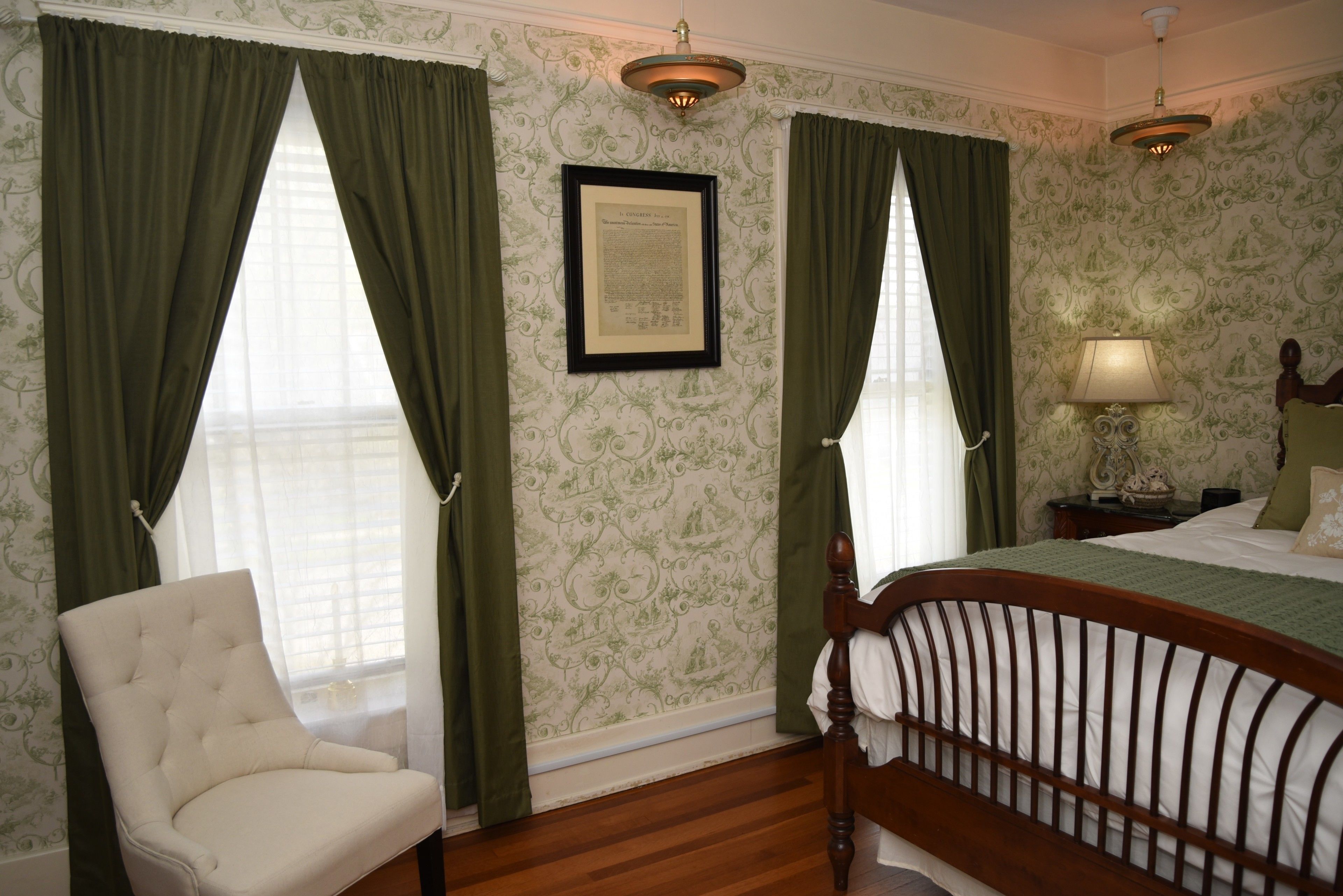 Un dormitorio con una cama de madera, un sillón blanco y cortinas verdes.