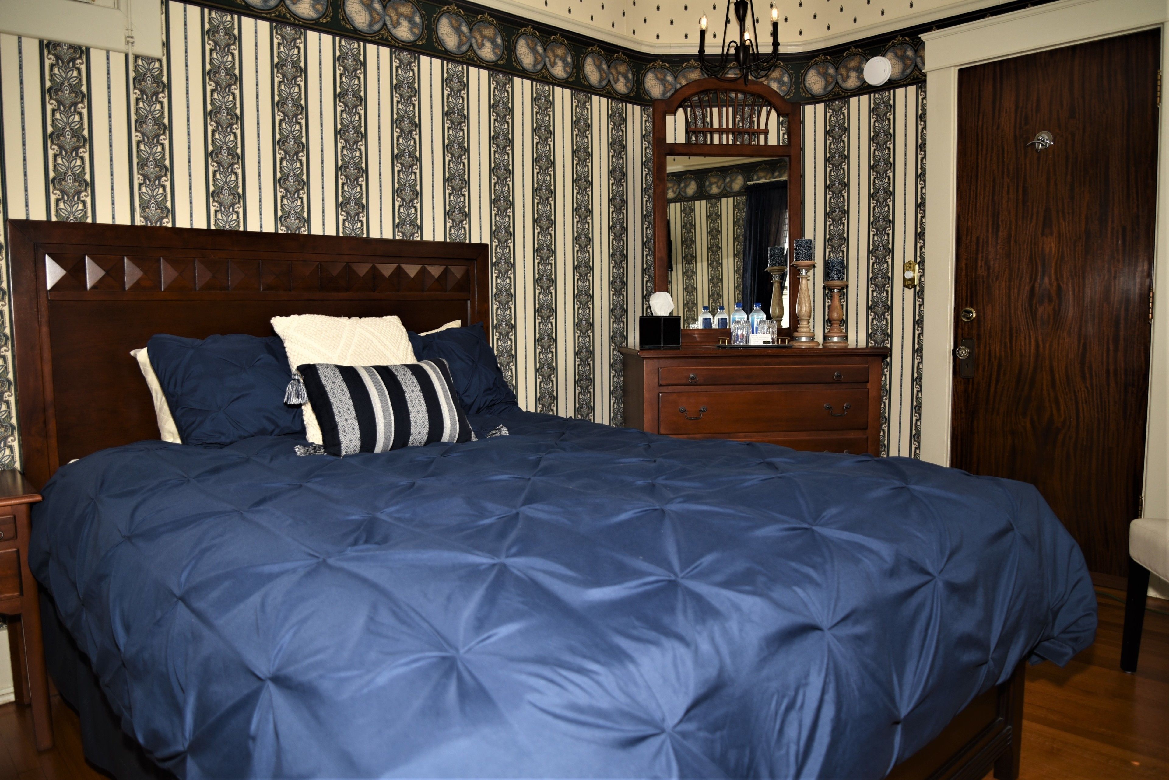 Une chambre à coucher avec un grand lit, une commode, un miroir et une porte.