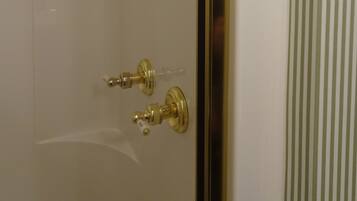 A bathroom with a white tiled wall, a gold showerhead, and a gold faucet.