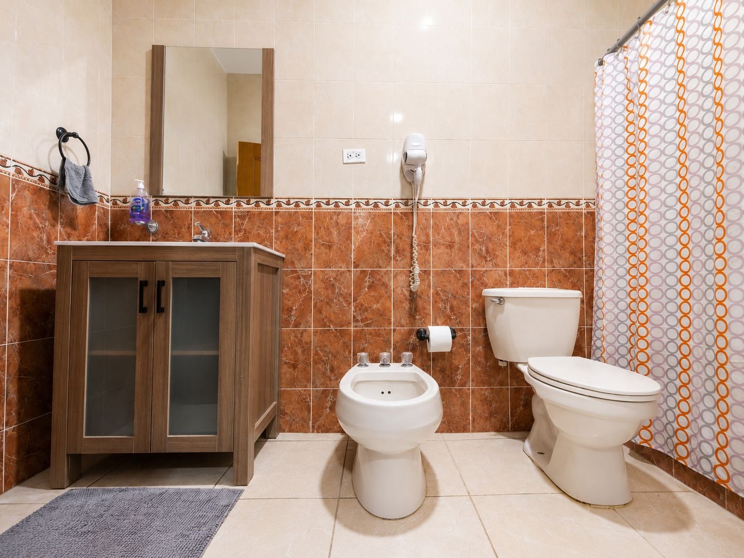 Une salle de bain avec un meuble en bois, un bidet, des toilettes, un porte-serviettes, un miroir et un rideau de douche.