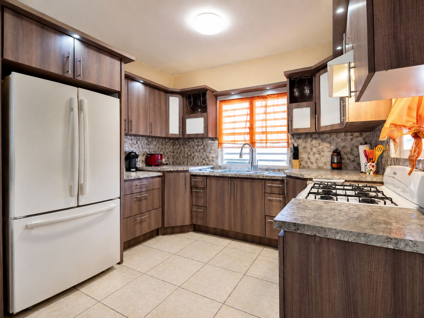 A modern kitchen with a refrigerator, stove, sink, and wooden cabinets.