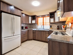 A modern kitchen with a refrigerator, stove, sink, and wooden cabinets. - Casa vacacional en Arenales Isabela (Isabela)