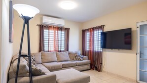 Un salon comprenant un canapé, un lampadaire, un téléviseur à écran plat et une porte-fenêtre coulissante.