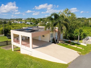 A modern house with a flat roof, a covered patio, and a paved driveway. - Casa vacacional en Arenales Isabela (Isabela)