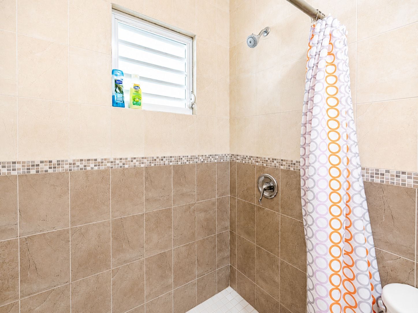 Ein Badezimmer mit Dusche, Fenster und Ablage für Toilettenartikel.