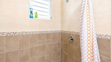 A bathroom with a shower, a window, and a shelf with toiletries.