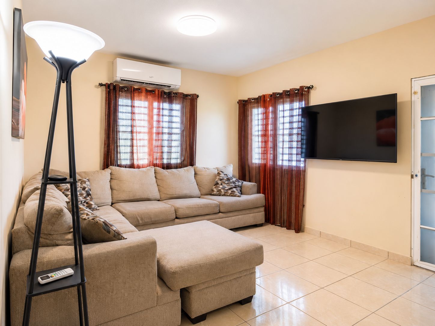 Un salon comprenant un canapé, un pouf, une lampe sur pied et un téléviseur à écran plat.