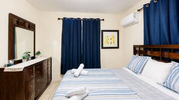 A hotel room with a bed, a dresser, a mirror, a painting, and blue curtains.