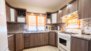 Une cuisine moderne avec des meubles en bois, une cuisinière à gaz, un évier et une fenêtre agrémentée de rideaux orange.