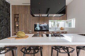 A modern kitchen with a central island, black bar stools, and a stone accent wall. - Villa Anar (Koh Samui)