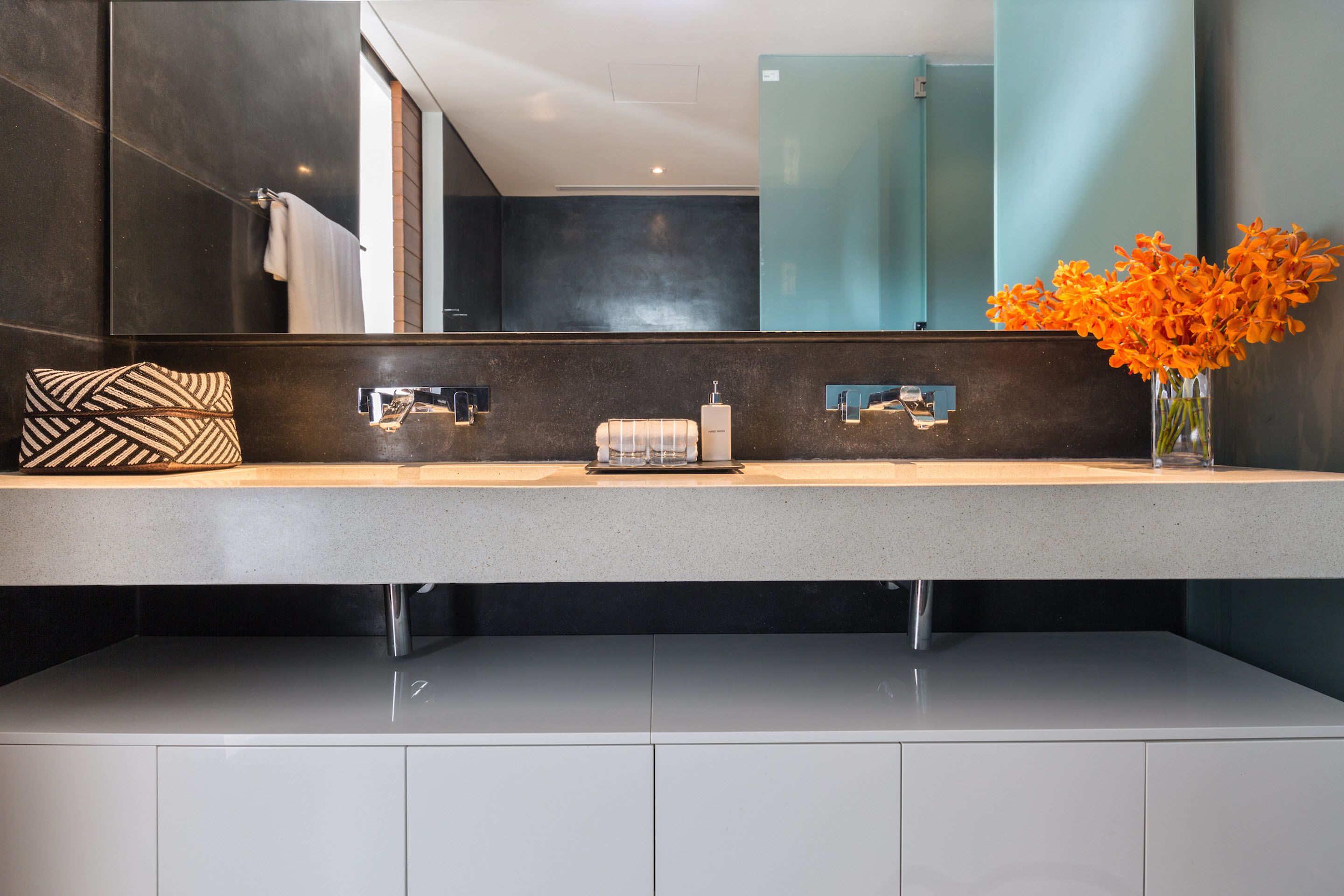 A modern bathroom with a dual sink vanity, a large mirror, and a vase with orange flowers.