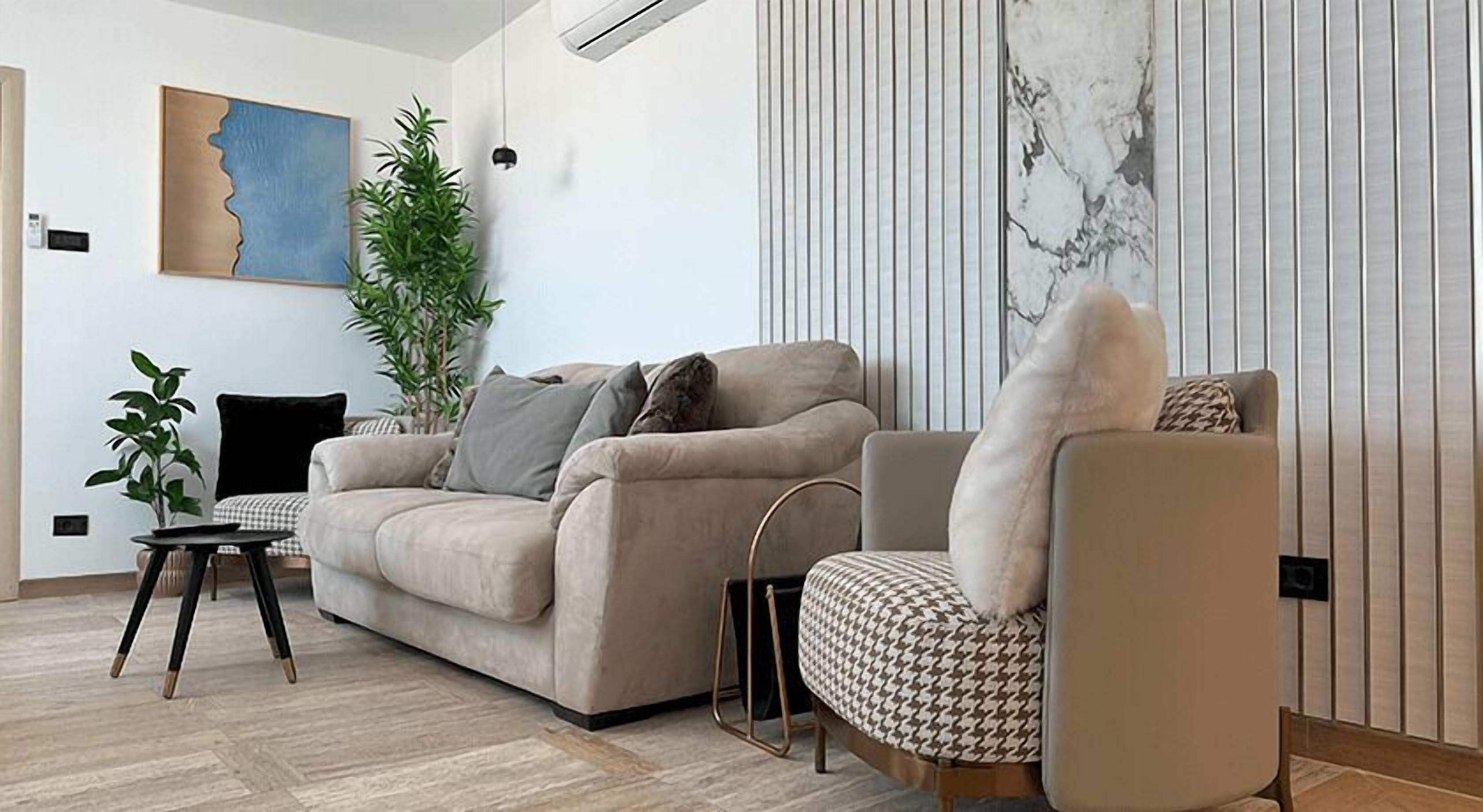 A modern living room with a beige sofa, a patterned armchair, a small side table, and a large potted plant.