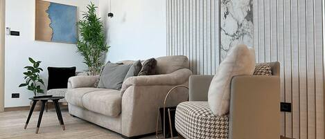 A modern living room with a beige sofa, a patterned armchair, a small side table, and a large potted plant.