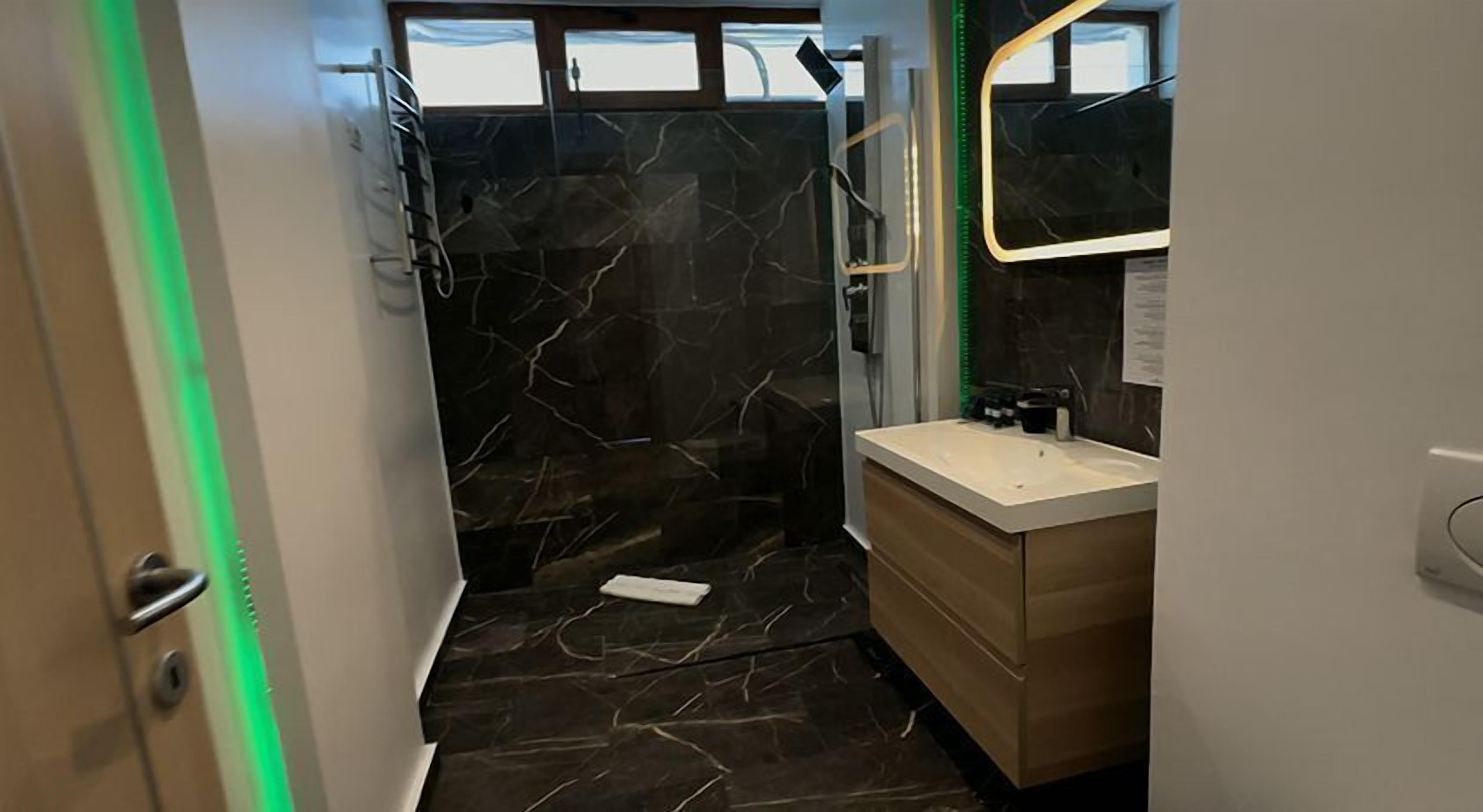 Un baño moderno con pared de ducha de mármol, tocador de madera y espejo.