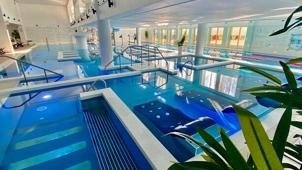 An indoor swimming pool with multiple lanes, a diving board, and a lifeguard stand. - Aqvatonic Balneo Spa - Steaua de Mare (Eforie)