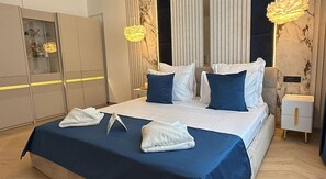 A modern bedroom with a large bed, white bedding, and a blue accent. There are two bedside tables, a wardrobe, and a mirror.