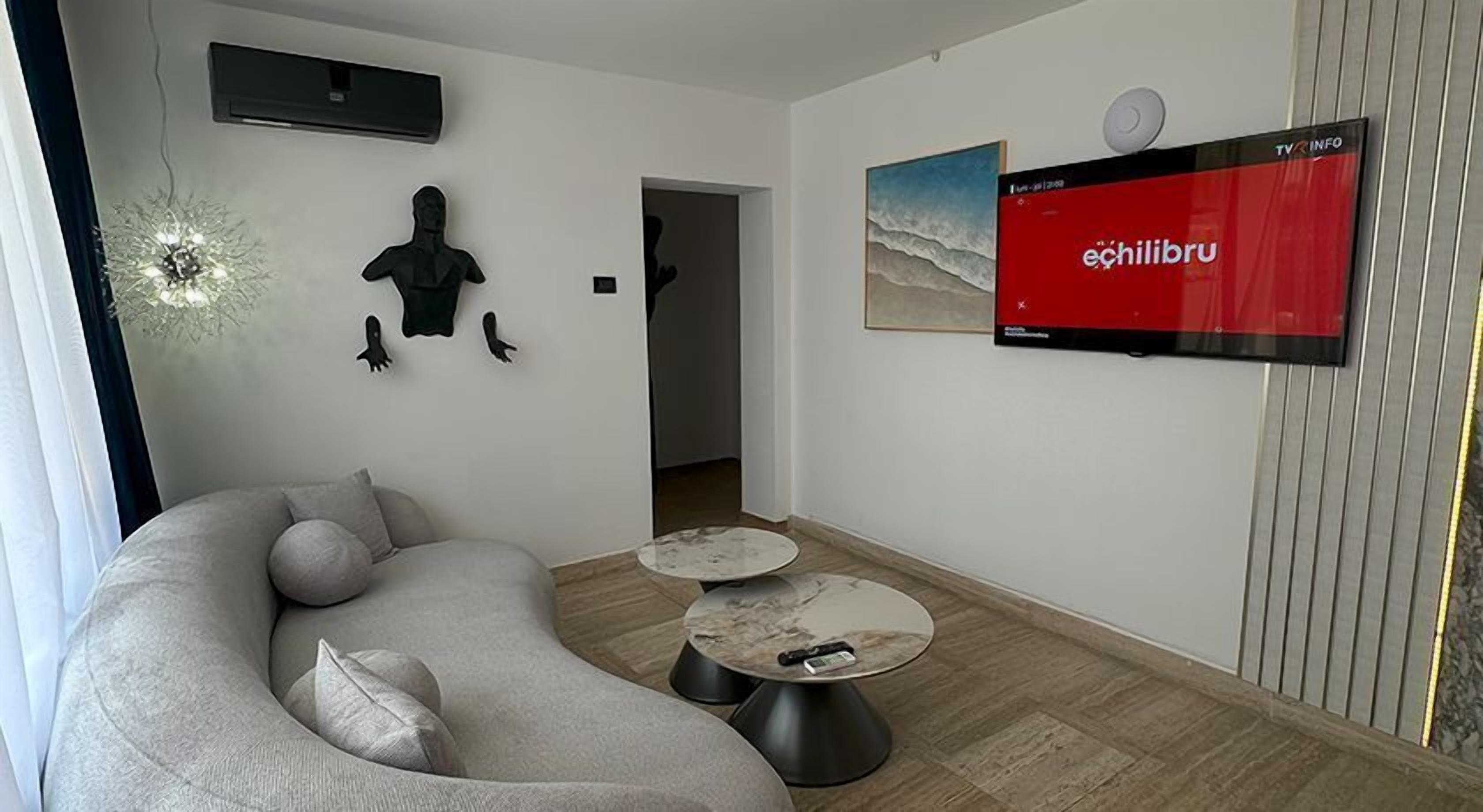 Una sala de estar moderna con un sofá modular, dos mesas de centro redondas y un televisor de pantalla plana mostrando 'echilbru'.