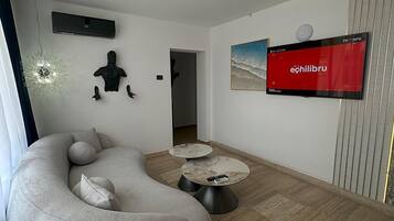 Una sala de estar moderna con un sofá modular, dos mesas de centro redondas y un televisor de pantalla plana mostrando 'echilbru'.
