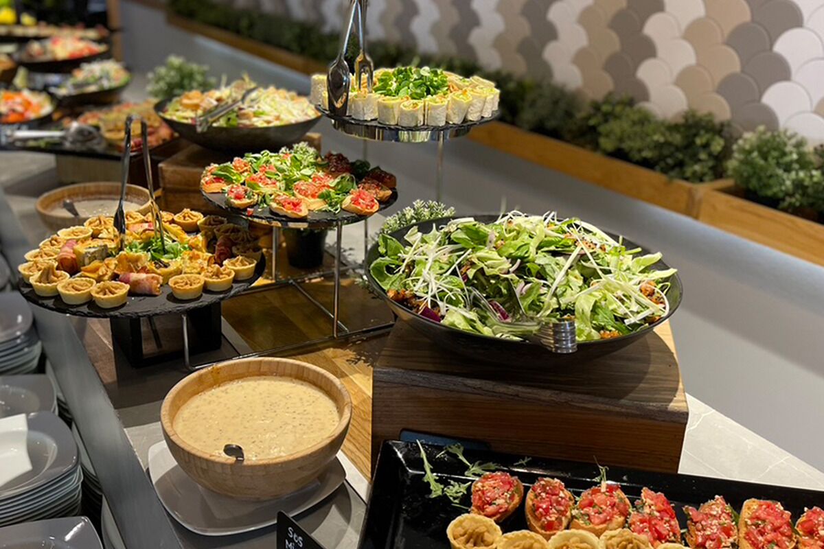 Un bufé con diversos alimentos, incluyendo ensaladas, aperitivos y un tazón grande de sopa.