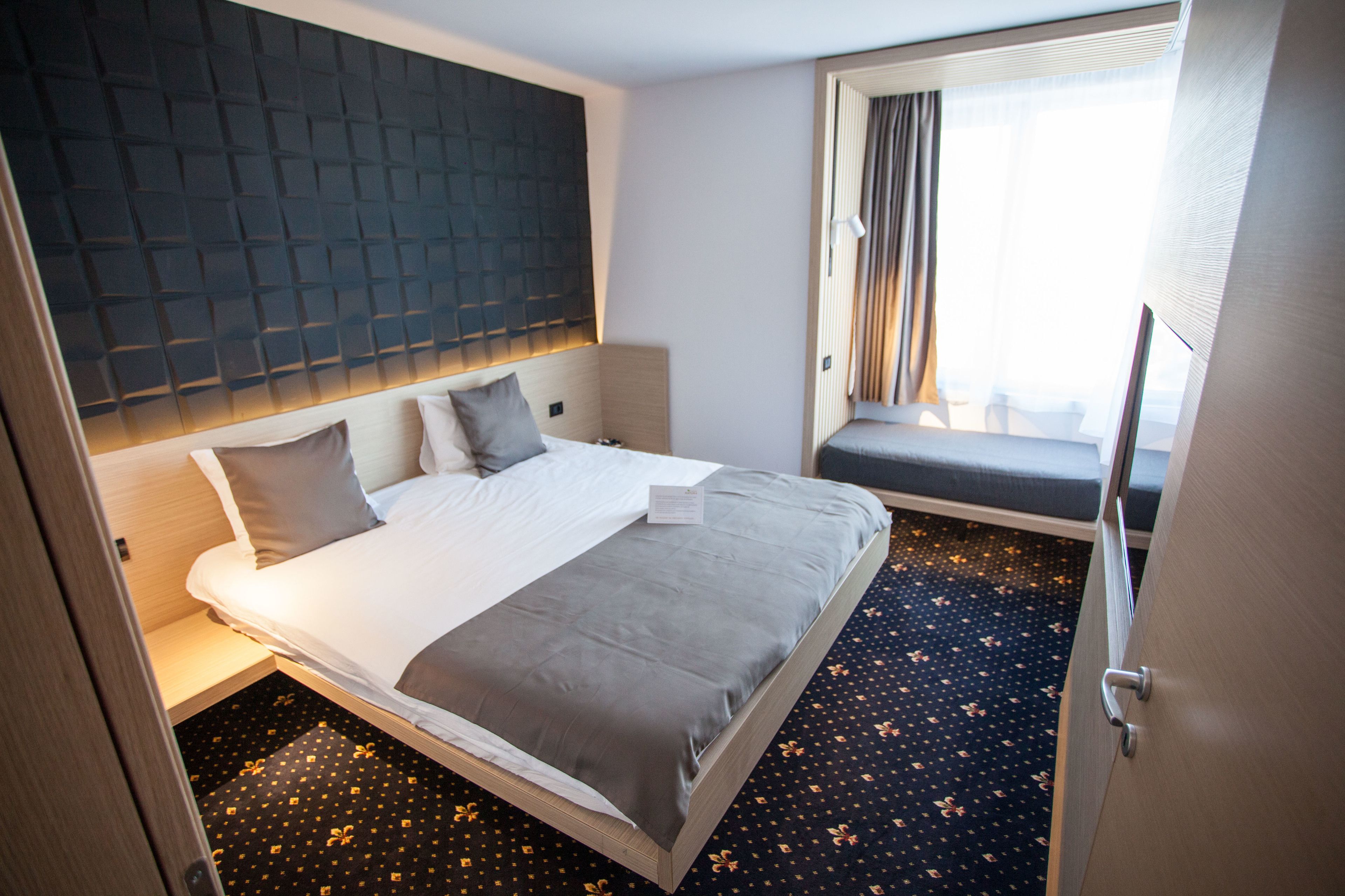Une chambre d’hôtel avec un grand lit, une tête de lit, une fenêtre avec des rideaux et un petit coin salon.