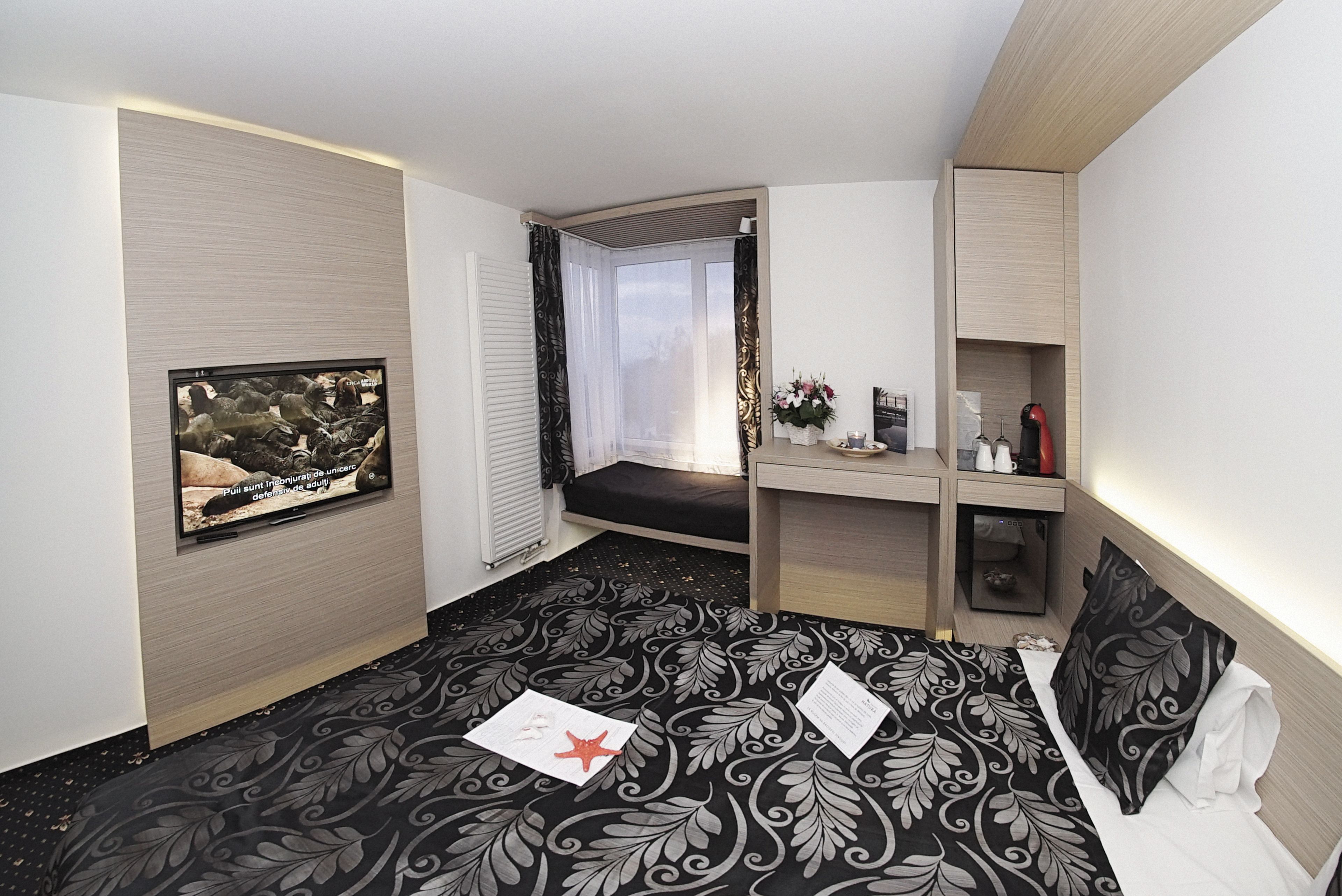 Een hotelkamer met een bed, een bureau, een stoel, een raam en een tv aan de muur.