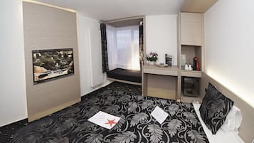 Een hotelkamer met een bed, een bureau, een stoel, een raam en een tv aan de muur.