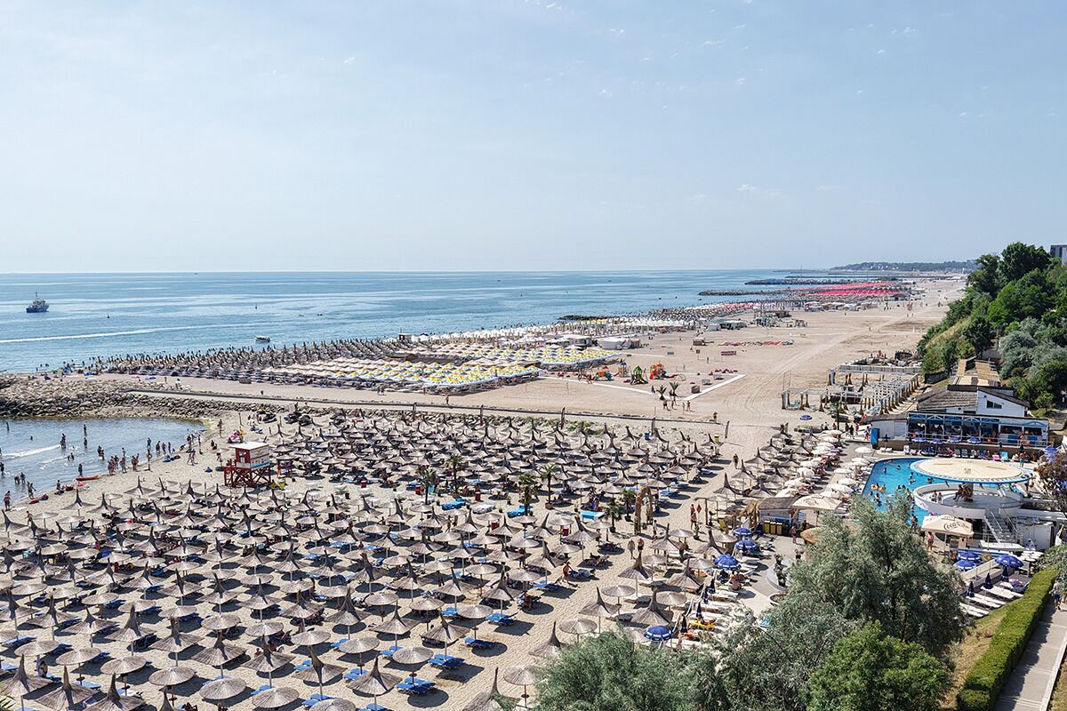 A beach resort with numerous umbrellas and sun loungers, a swimming pool, and a large beach area.