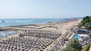 A beach resort with numerous umbrellas and sun loungers, a swimming pool, and a large beach area.