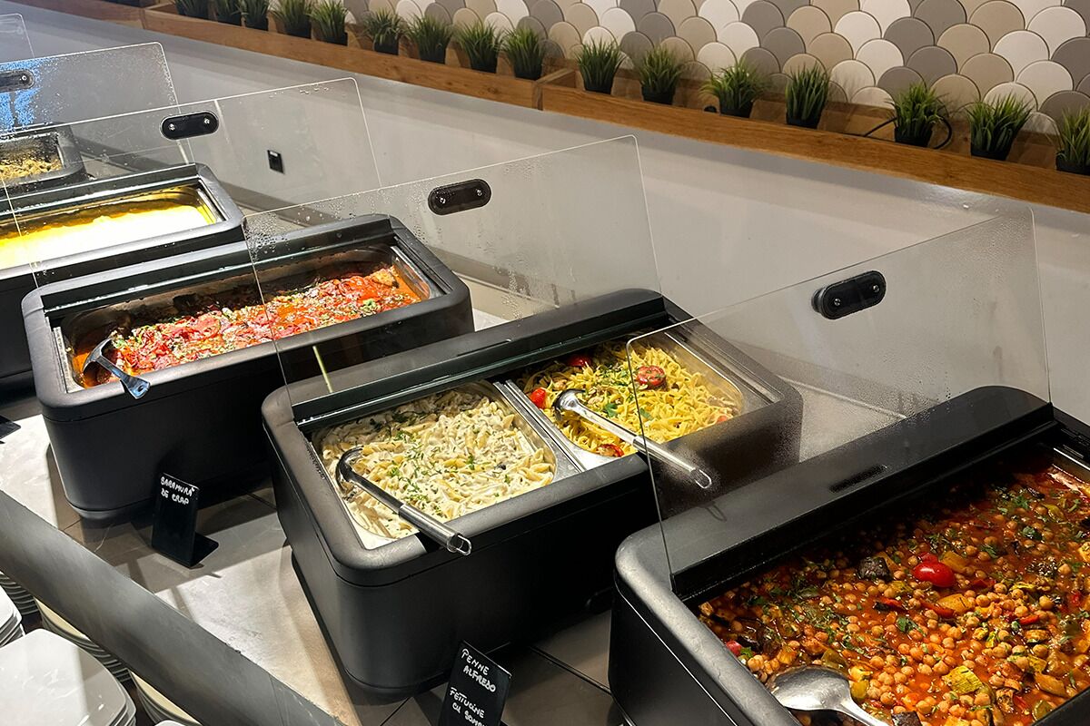 Un bufé con diversos platos, como pasta, ensaladas y un guiso de verduras.