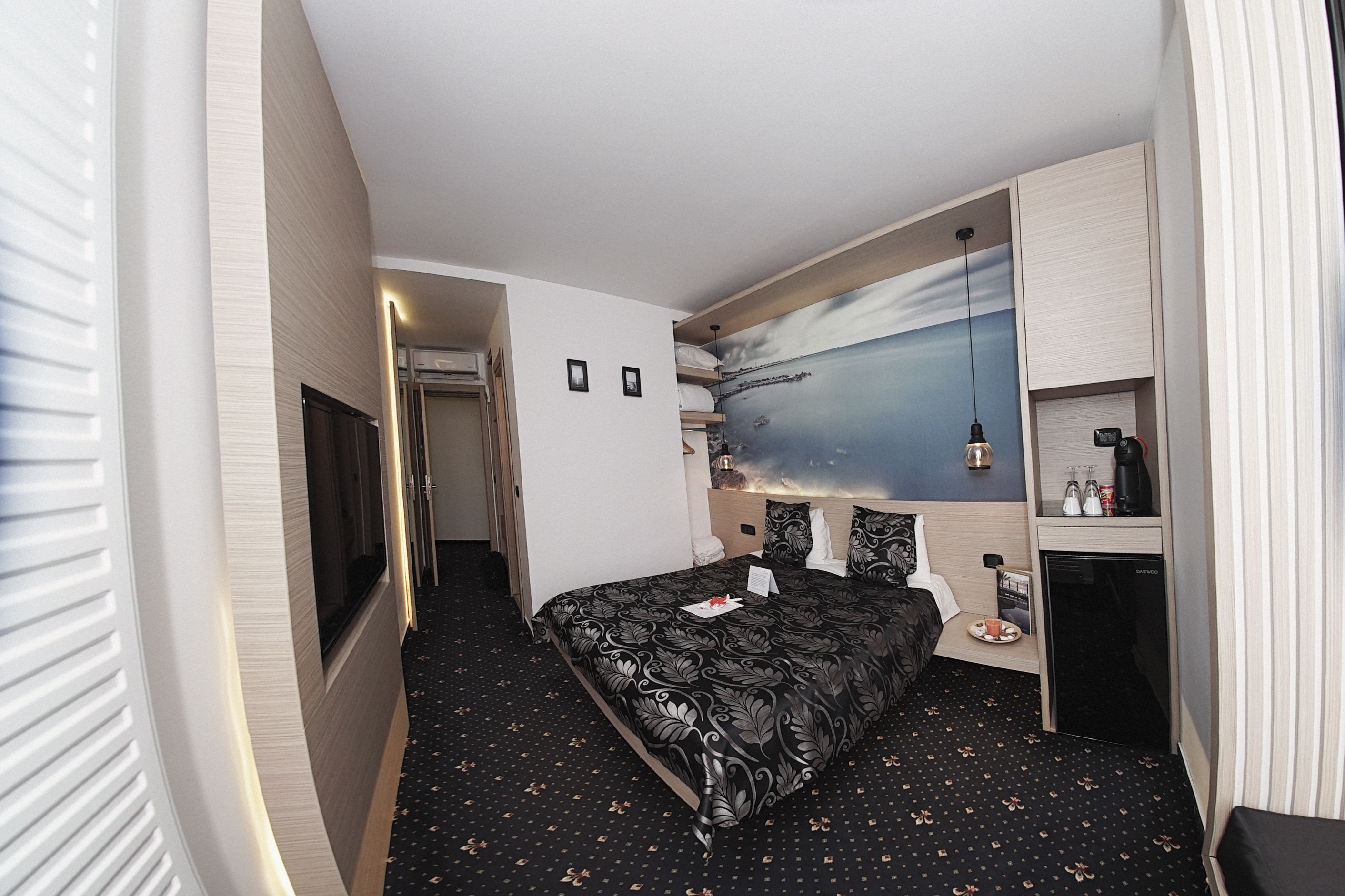 Una habitación de hotel con cama, escritorio, refrigerador pequeño y televisor montado en la pared.