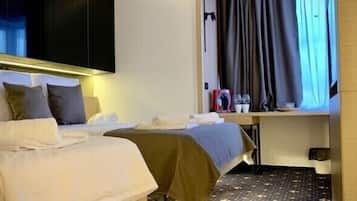 Camera d'albergo con due letti, una scrivania e un'ampia finestra con tende.