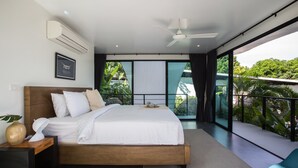 Une chambre moderne avec un grand lit, un ventilateur de plafond et une vue sur une végétation luxuriante.