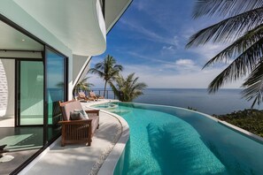 Una piscina infinita moderna con vista despejada al océano, un banco de madera y una puerta de vidrio que da a una habitación.
