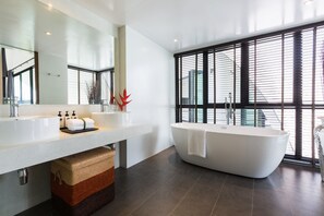 Un baño moderno con una bañera independiente, un espejo grande y una ventana con persianas.