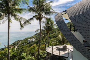 Un edificio moderno con techo curvo que domina una zona costera con palmeras y vista al mar.