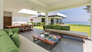 Uma sala de estar moderna com uma grande janela com vista para uma área gramada e o mar.