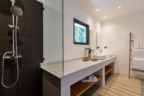 A modern bathroom with a glass shower enclosure, a white vanity with a mirror, and a wooden shelf. - Villa Thansamaay (Koh Samui)