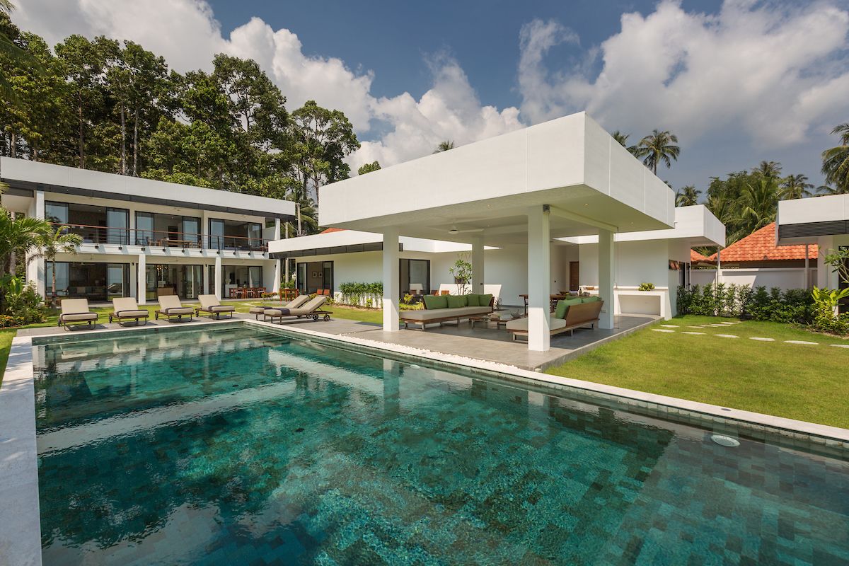 A modern poolside area with a clear pool, lounge chairs, and a covered seating area.