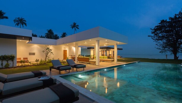 Uma casa moderna com piscina, cadeiras de sol e um espaço coberto de varanda.