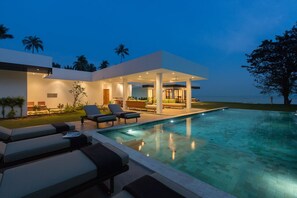 Une maison moderne dotée d’une piscine, de chaises longues et d’un patio couvert.