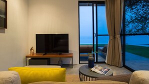 Uma sala de estar moderna com televisão de tela plana, sofá, mesa de centro e vista para o oceano através de grandes portas de vidro.