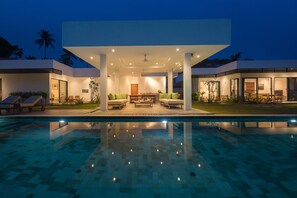 A modern outdoor pool area with a covered seating area, lounge chairs, and a well-lit patio. - Villa Thansamaay (Koh Samui)