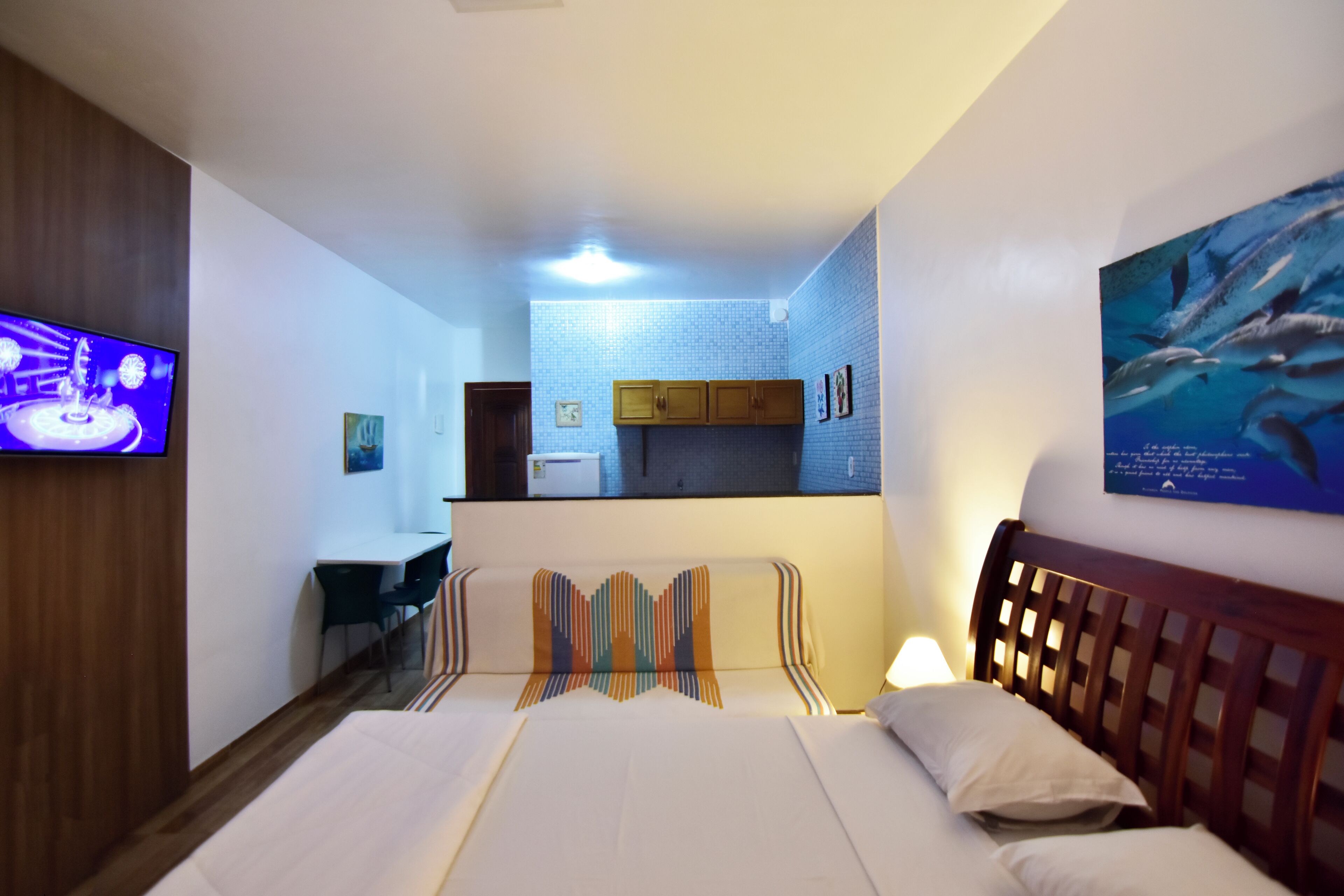 A hotel room with two beds, a TV, a desk, and a kitchenette.