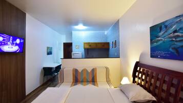 A hotel room with two beds, a TV, a desk, and a kitchenette.