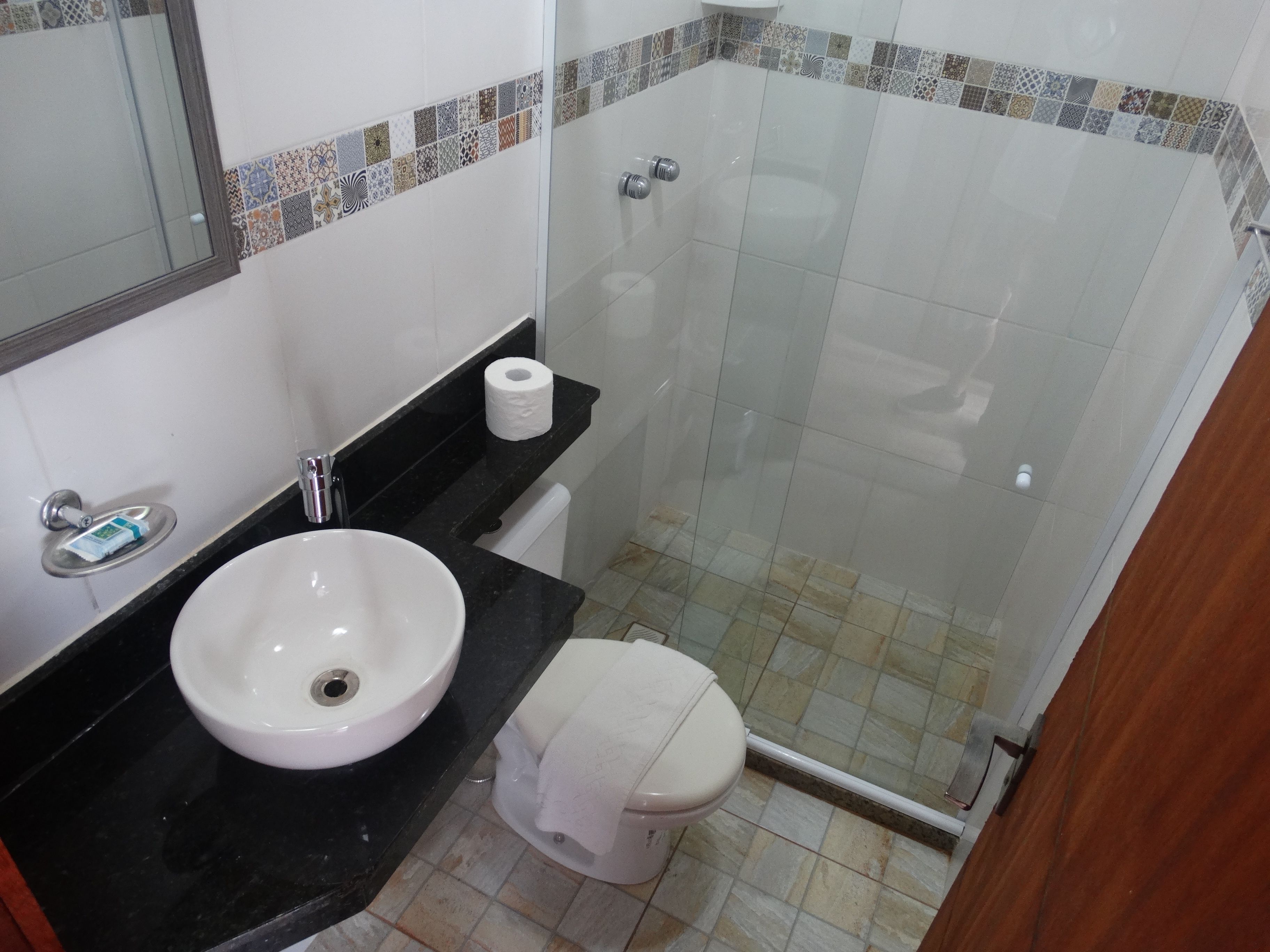 Une salle de bain avec un lavabo blanc, un plan de toilette noir, des toilettes et une douche à parois de verre.