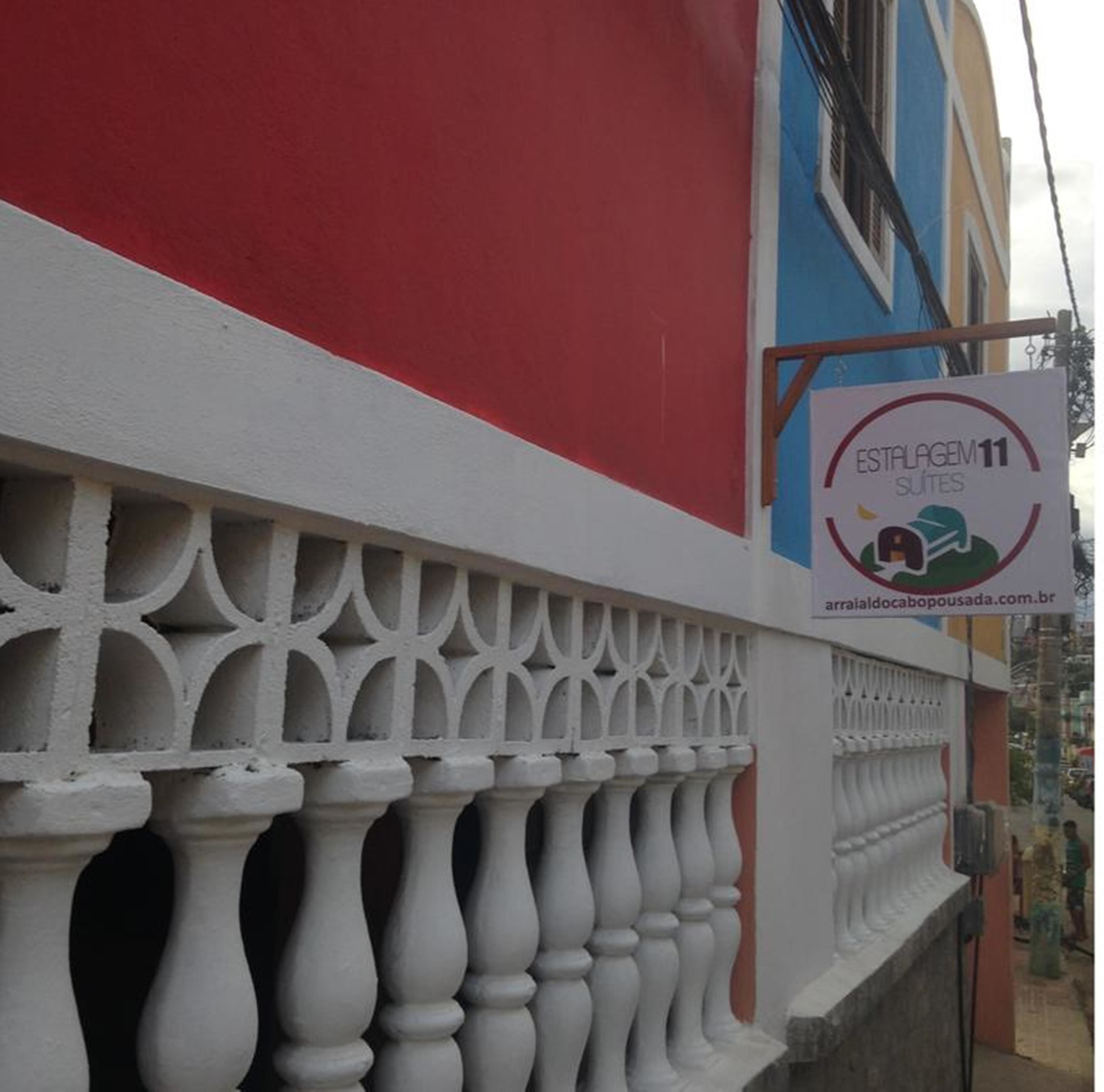 A building with a red and white facade, a balcony with white balustrades, and a sign advertising 'Estalagem 11 Suites' with a website URL.