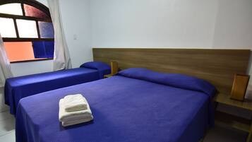 A hotel room with two single beds, each with a blue bedspread and pillows, a wooden headboard, and a window with curtains.